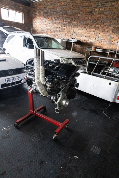 A rebuilt BMW engine on a stand beside a kit-car chassis