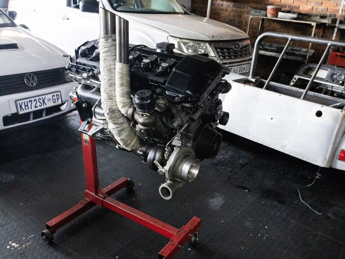 A rebuilt engine on a stand beside the kit-car chassis at CRS Auto